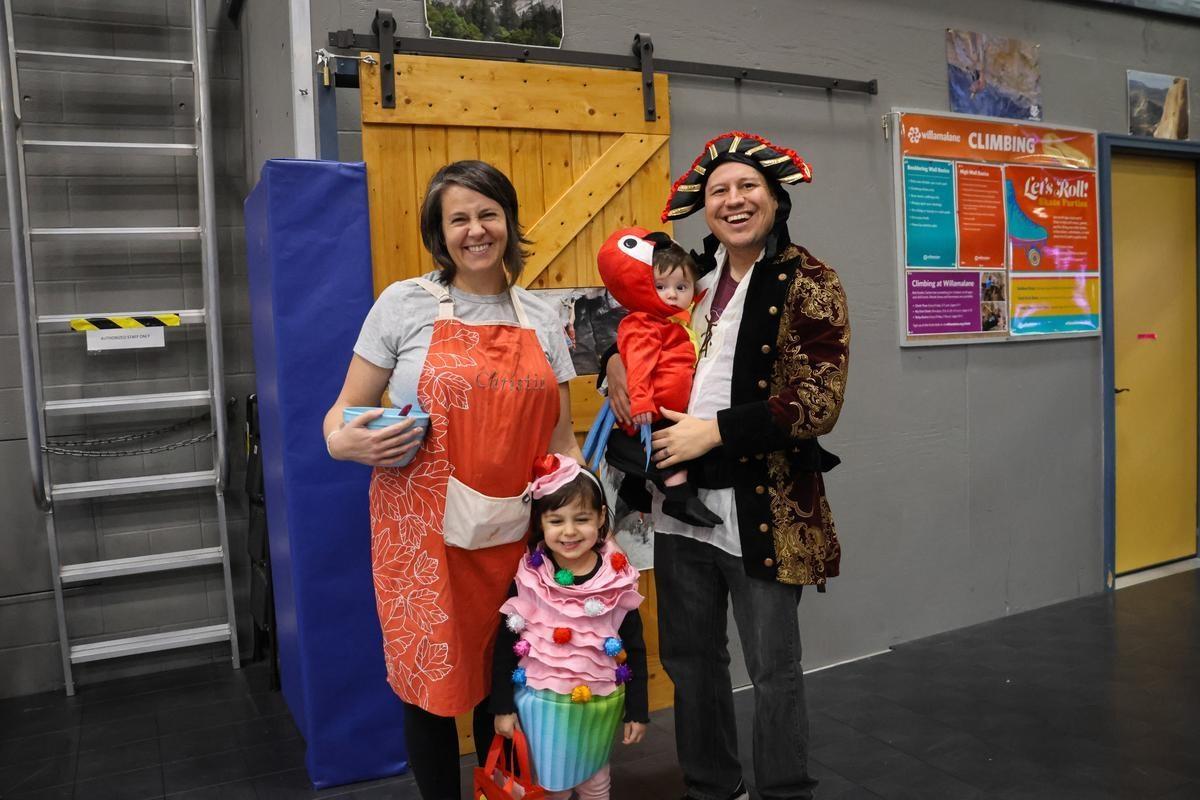 A family in halloween costumes stands in front of a wood door.