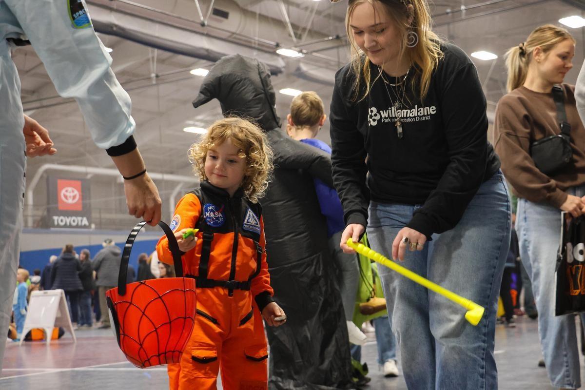 A child in an astronaut costume reaches for a bucket of candy.