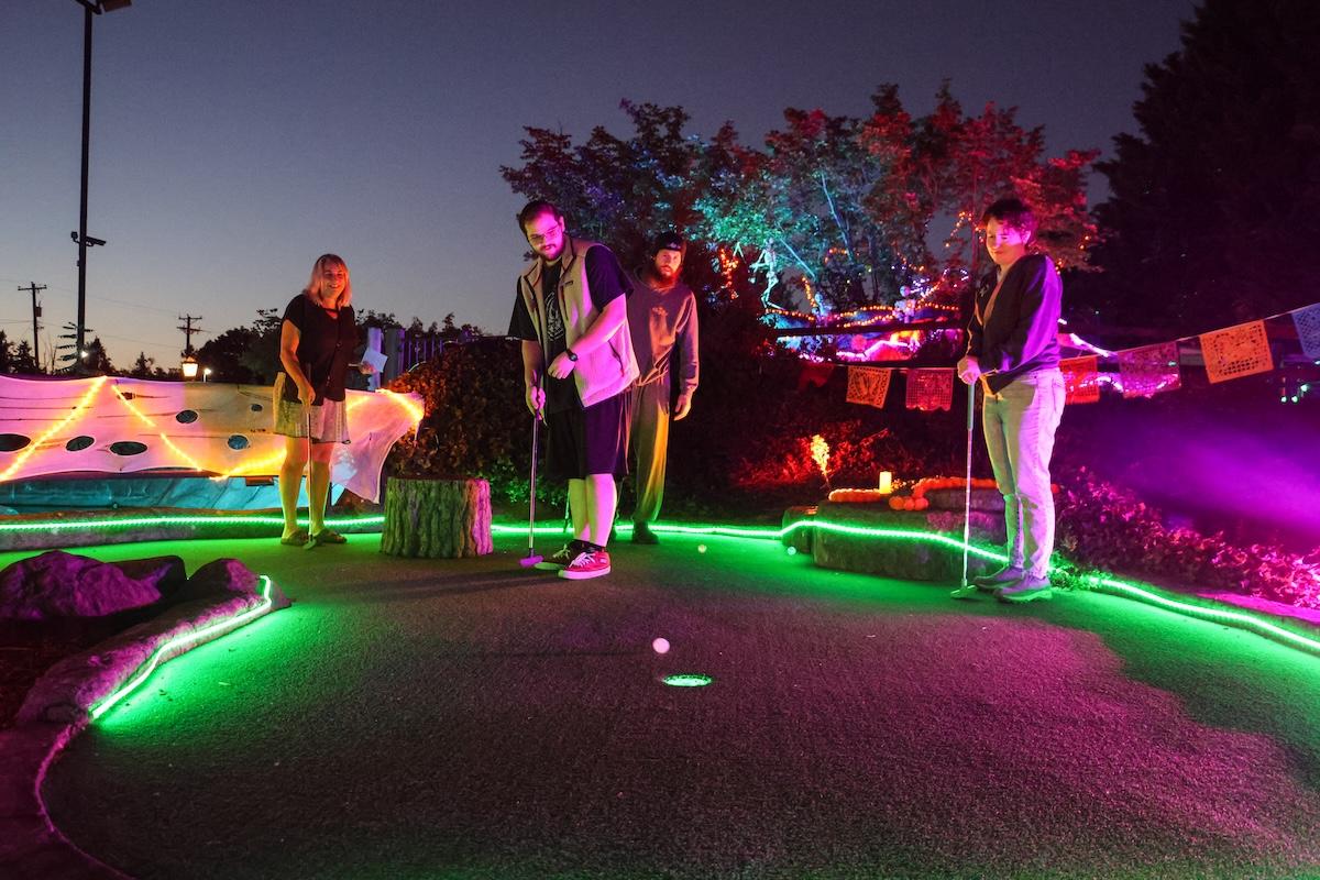 A group of mini golfers standing on the green at dusk.