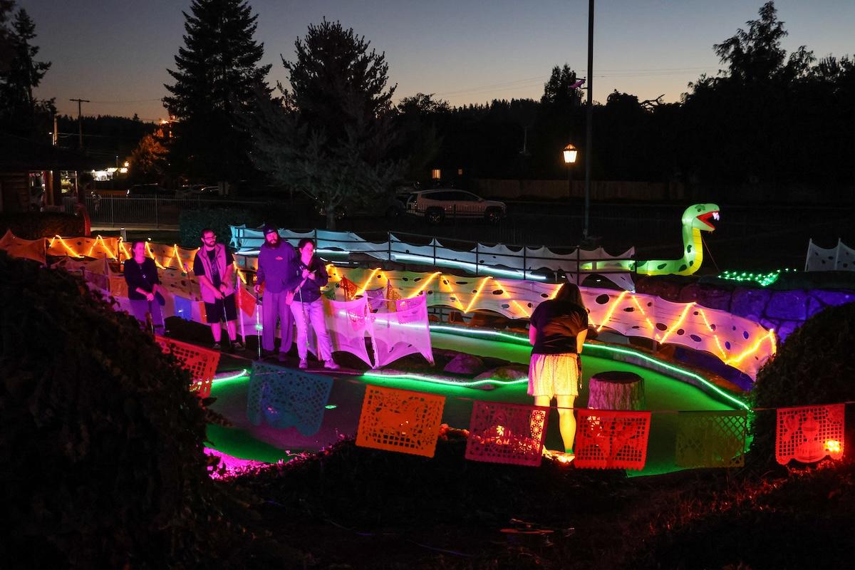 A mini golf course at night with colorful lights and decorations.