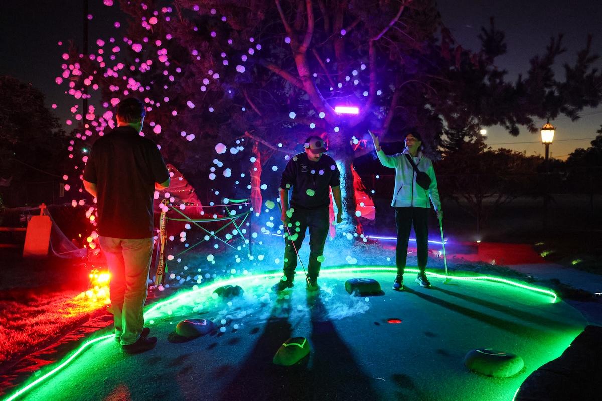Three mini golfers illuminated on the course at night. 