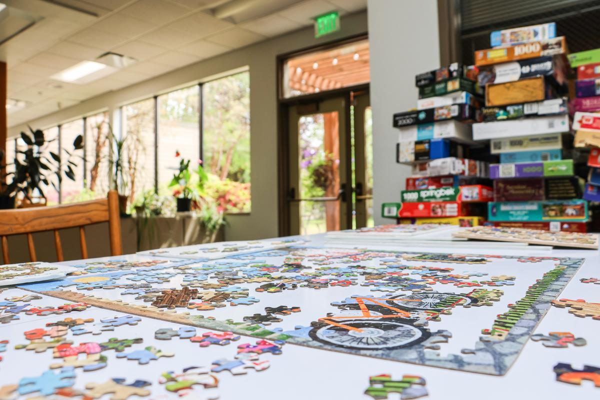 An unfinished puzzle with stacks of games and books behind.