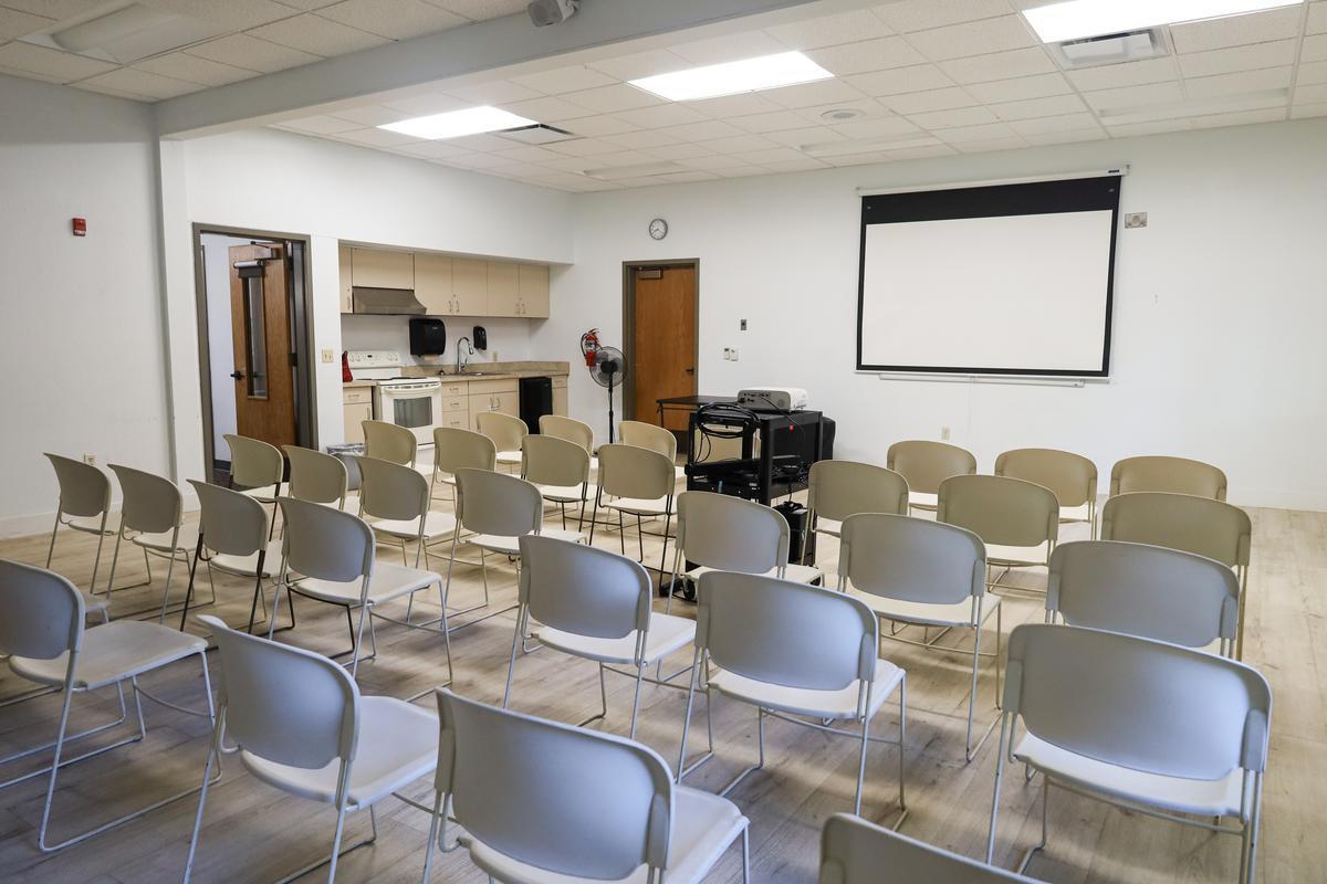 An empty room with rows of chairs in front of a projector screen.