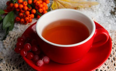 A cup of tea sits steaming on a red plate with red holiday berries.