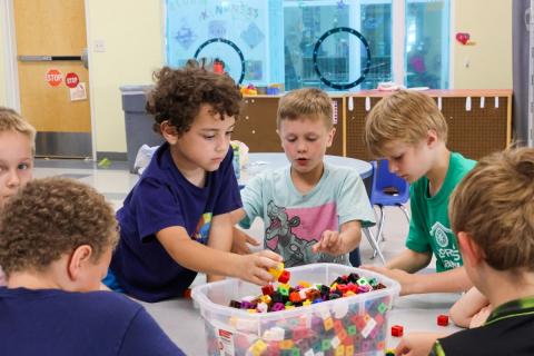 A group of children sitting around a plastic bin filled with colored Legos.