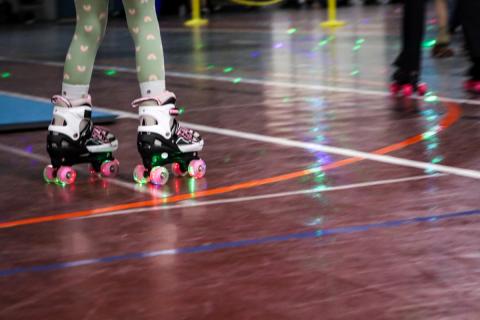 A pair of rollerskates with glowing lights on the wheels glides on top of a brown floor.